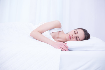 Young beautiful smiling woman is sleeping sweetly in a white bed at home. Relax and rest.