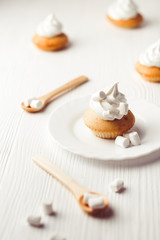 Cupcakes with vanilla cream and marshmallow on white plate, on wooden backdrop, vertical composition