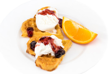 Plate of belgian waffles with ice cream, jam and a slice of orange on white background