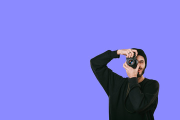 Stylish digital photographer with a beard in black shirt and casual hat. Isolated on blue background, white place for your descripition concept.