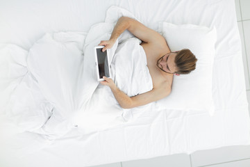 smiling man using digital tablet lying on bed