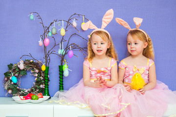 two beautiful little girls dressed in pink lush and rabbit ears decorate the house with decorative eggs