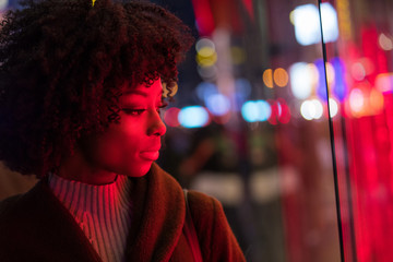 Fototapeta premium Pretty African American Woman with red light on her face at night in city