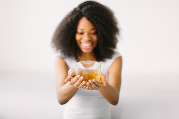 An African American young woman sitting in the lotus position on white bed with cup of tea