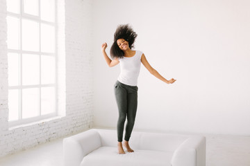 Fototapeta premium An African American young woman jumping on white bed