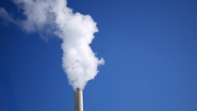 A Smoke stack blowing smog or water vapor our of tower on clear sky backdrop - Close Up