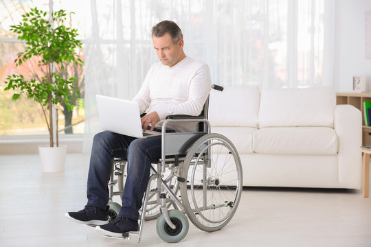 Mature man in wheelchair using laptop indoors