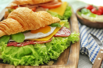 Wooden board with tasty croissant sandwich on table