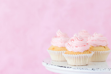Cupcake decorated with pink buttercream on shabby shic stand on pastel pink background.
