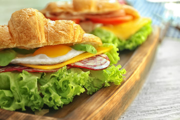 Wooden board with tasty croissant sandwich on table