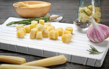 White cutting board with fresh young baby corn on table, closeup