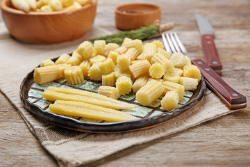 Plate with fresh young baby corn on wooden table