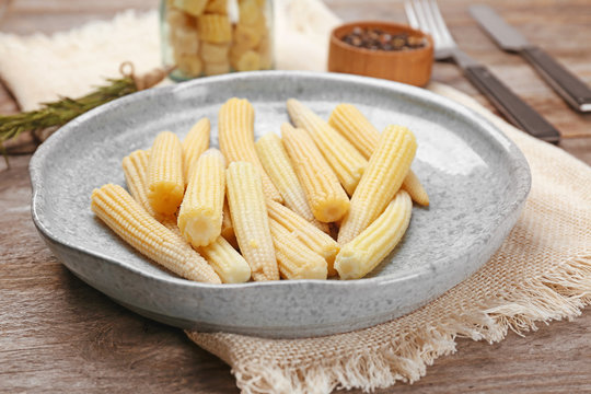 Plate with fresh young baby corn on wooden table, closeup