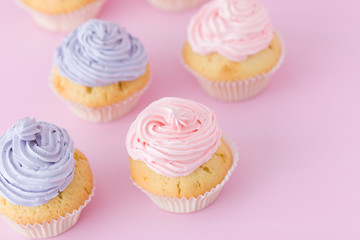 Violet and pink cupcakes with buttercream standing on pastel pink background.