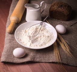Ingredients for bakery products - milk, eggs, flour and rolling pin - on a rustic wooden background.