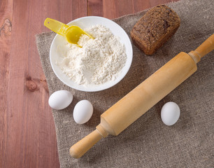 Fototapeta na wymiar Eggs, flour and rolling pin - on a rustic wooden background. Ingredients for bakery products