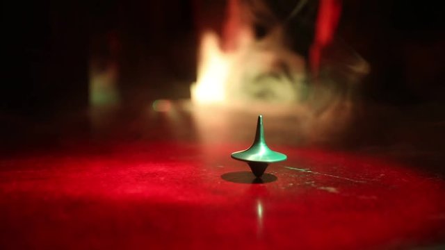 Totem spinning top spinning, wobbling and stopping. Spinning top on mirror surface with toned smoke background light. Whirligig in action in dark room on table. 