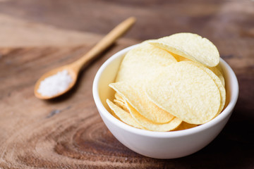 Potato chip in a bowl and spoon of salt on wooden background