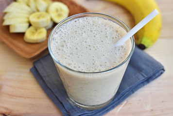 Smoothie with banana in the glass, fresh bananas on the wooden background