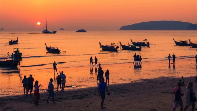 Time lapse of the Thai traditional beach with a lot of people silhouettes, moored Thai long-tail boats and yachts at sunset. Camera moves from top to bottom