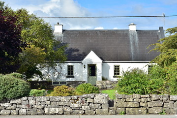 White Irish country cottage with high roof on property protected by low stone wall.