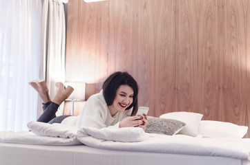 Happy girl using a mobile phone lying on the bed at home