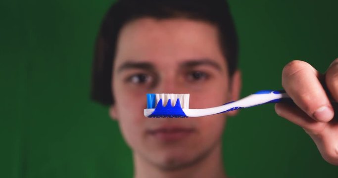 Handsome young guy (teenager) brushes teeth, green background.