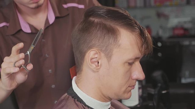 Close-up of barber cuts the hair by scissors at barbershop in slow motion.