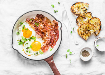 Traditional breakfast or snack - fried eggs, bacon, grilled bread on light background, top view. Flat lay