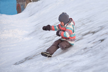 Fototapeta na wymiar Funny little kid boy in colorful clothes playing outdoors in winter on cold snowy days. Happy child having fun and playing with snow