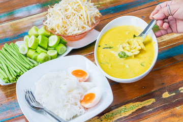 Rice vermicelli in green curry with crab and vegetables with Long bean and hoary basil on wooden table the traditional delicious Thai food.
