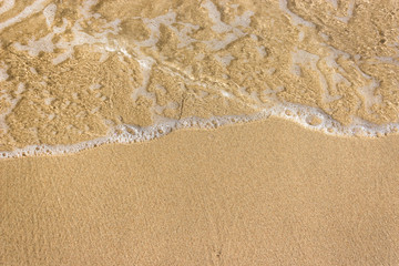 Fototapeta na wymiar Soft waves with foam of ocean on the sandy beach background