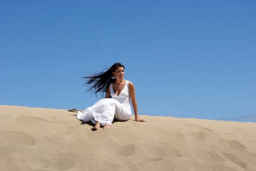 Fototapeta na wymiar Beautiful brunette young woman bride sitting in sand dunes with the sky background