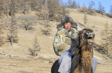 nomad man wearing a wolf skin jacket, riding his horse in a steppe in Northern Mongolia