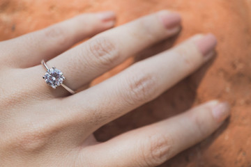 Close up of an elegant diamond ring on woman finger with .red clay background. soft and selective focus. Love and wedding concept.