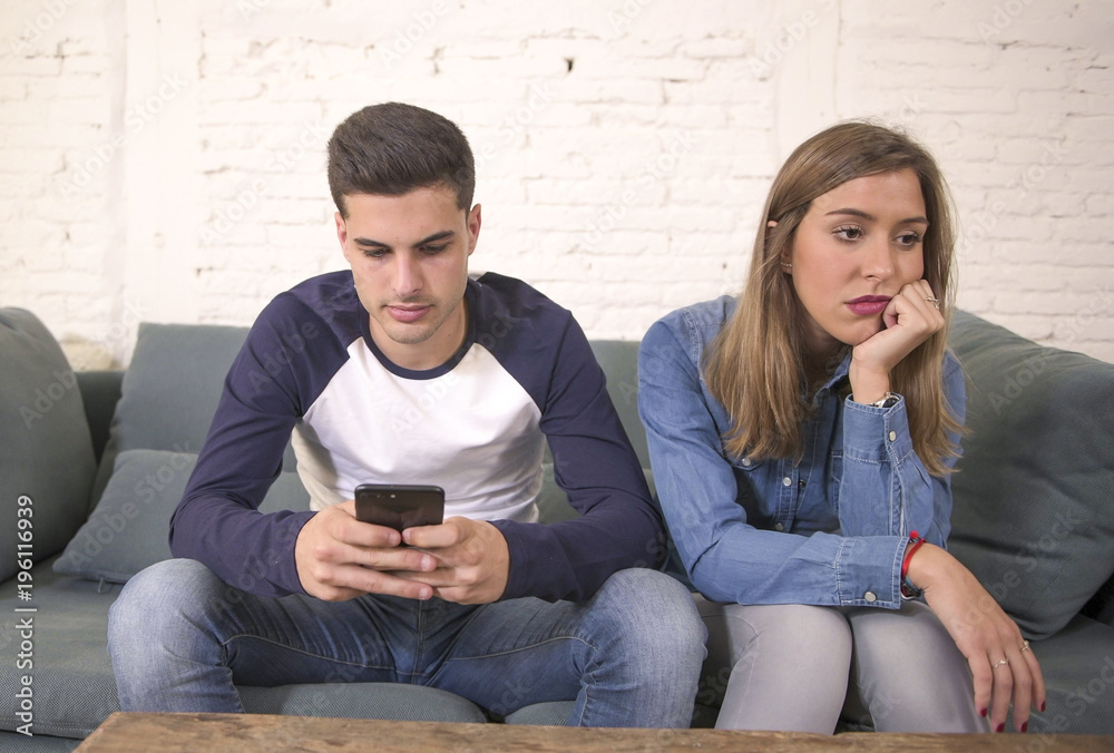 Wall mural young attractive couple in relationship problem with internet mobile phone addiction boyfriend ignoring sad neglected and bored girlfriend