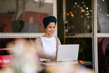 Portrait of a slim, young Muslim Malay woman sitting and working at a cafe during the day. She is...