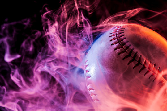 Close up of a white baseball ball in multi-colored red smoke from a vape on a black isolated background