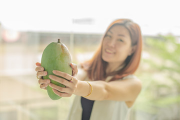 Fototapeta premium woman holding a fresh Mango in her hand and blur of woman