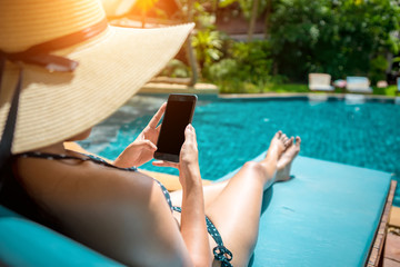An Asian woman sitting at the swiming pool and using the smart phone to check here work email or social media.