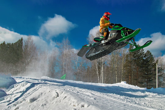 Big green Sport snowmobile jump. Cloud of snow dust from under snowmobile tracks. Concept extreme rest.