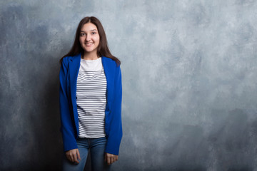 Fototapeta premium A young pretty smiling girl against a modern gray loft-style wall. She looks at the viewer. Copy space.