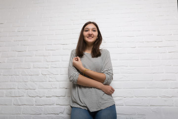 A young pretty smiling girl against a white loft-style brick wall. She looks at the viewer. Copy space.