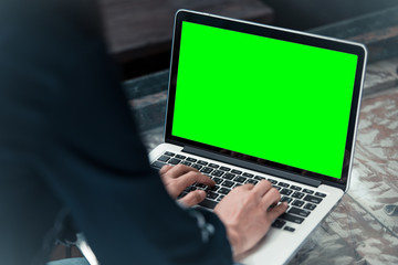 Woman using laptop with blank green screen.