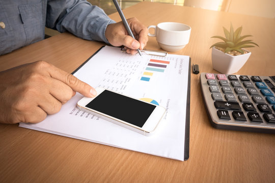 Business man analyzing investment charts with smart phone and calculator on office desk table.Close up.Financial Report Revenue Statistical Accounting Concept.