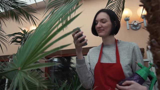 Young smiley girl in red apron laughing using smartphone in house garden.