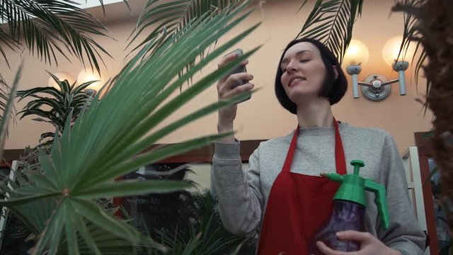 Young smiley girl in red apron taking selfie using smartphone in orangery