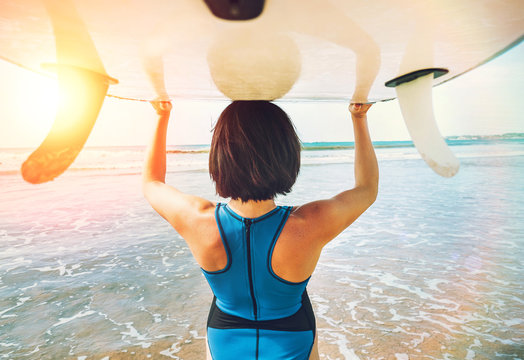 Woman takes surfboard on head and goes in ocean waves