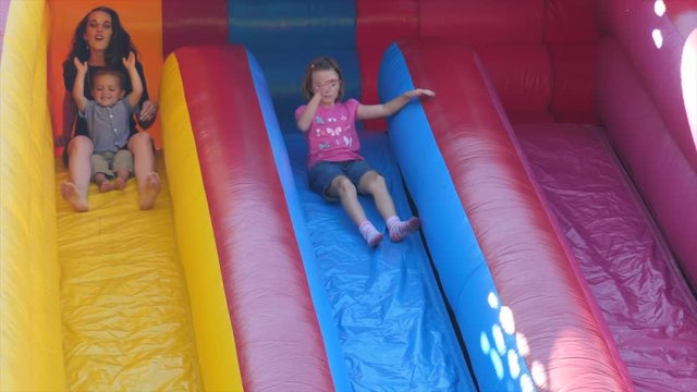 Slow motion family slides down a huge inflatable slide during a party