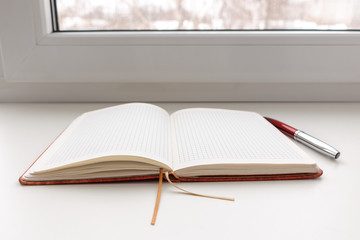 Open blank notebook with red ballpoint pen on white window sill